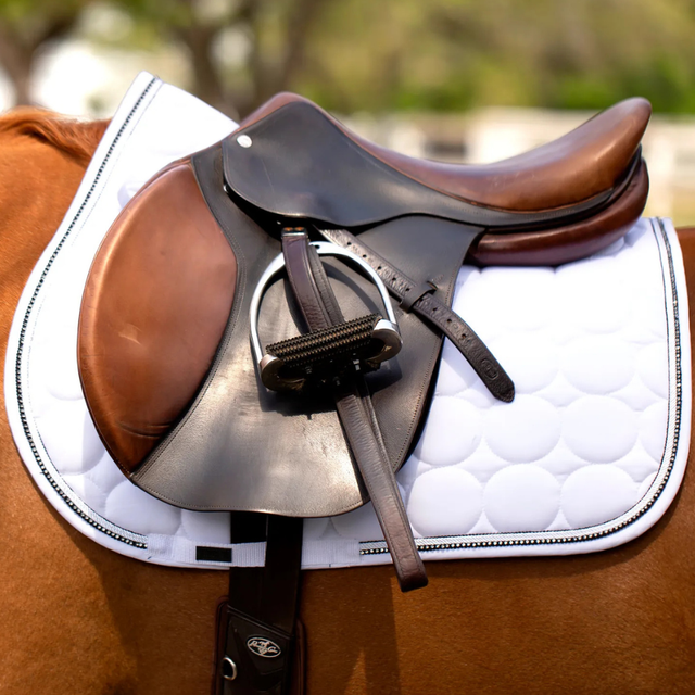Brown saddle on a horse with a white saddle pad outdoors