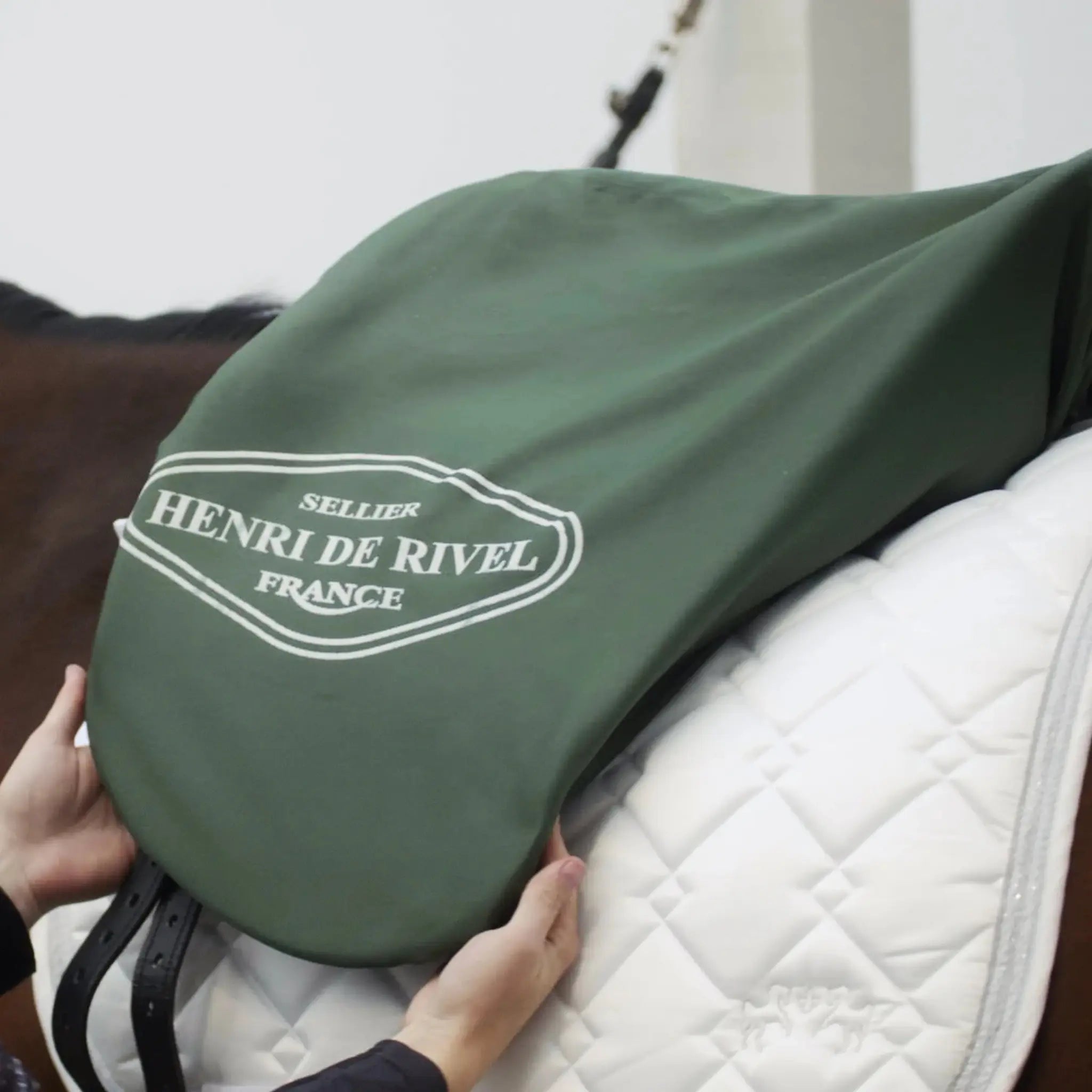 Green Henri de Rivel saddle cover being held over a white saddle pad on a horse.