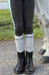 Person wearing black riding boots and gray socks with 'TuffRider' branding, standing next to a horse.